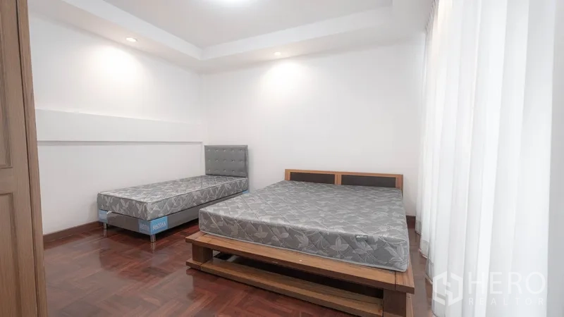Townhouse for rent in Watthana, Bangkok - Guest bedroom with two beds and wood flooring.