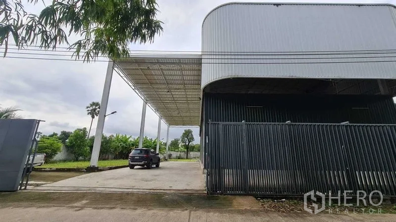 Warehouse for rent in Mueang Nonthaburi, Nonthaburi - Side perspective of the warehouse showing an extended roof canopy and secure fence line.