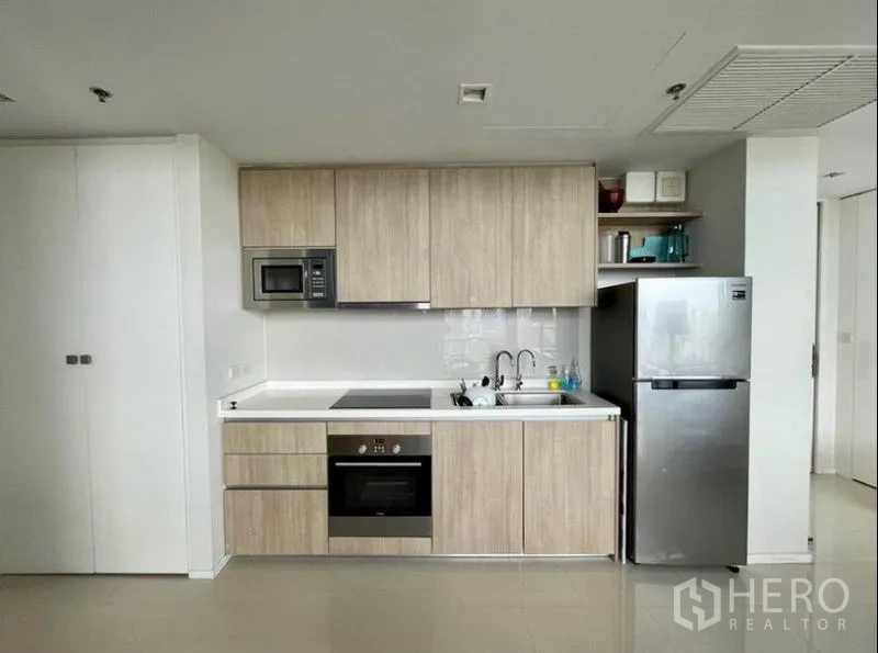 Condominium for sale in Ratchathewi, Bangkok - Light-wood kitchenette with built-in oven, cooktop, microwave, and fridge.