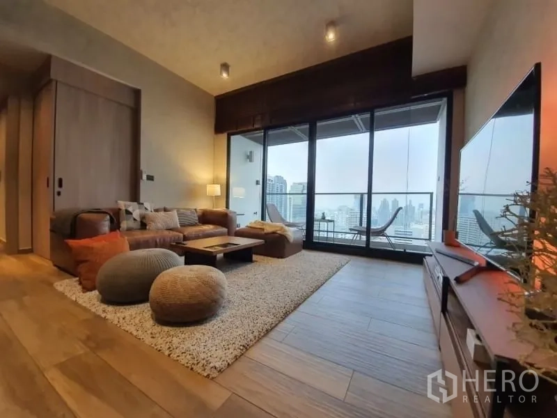 Condominium for rent or sale in Watthana, Bangkok - Living area opening to a balcony with floor‑to‑ceiling glass and Bangkok skyline views.