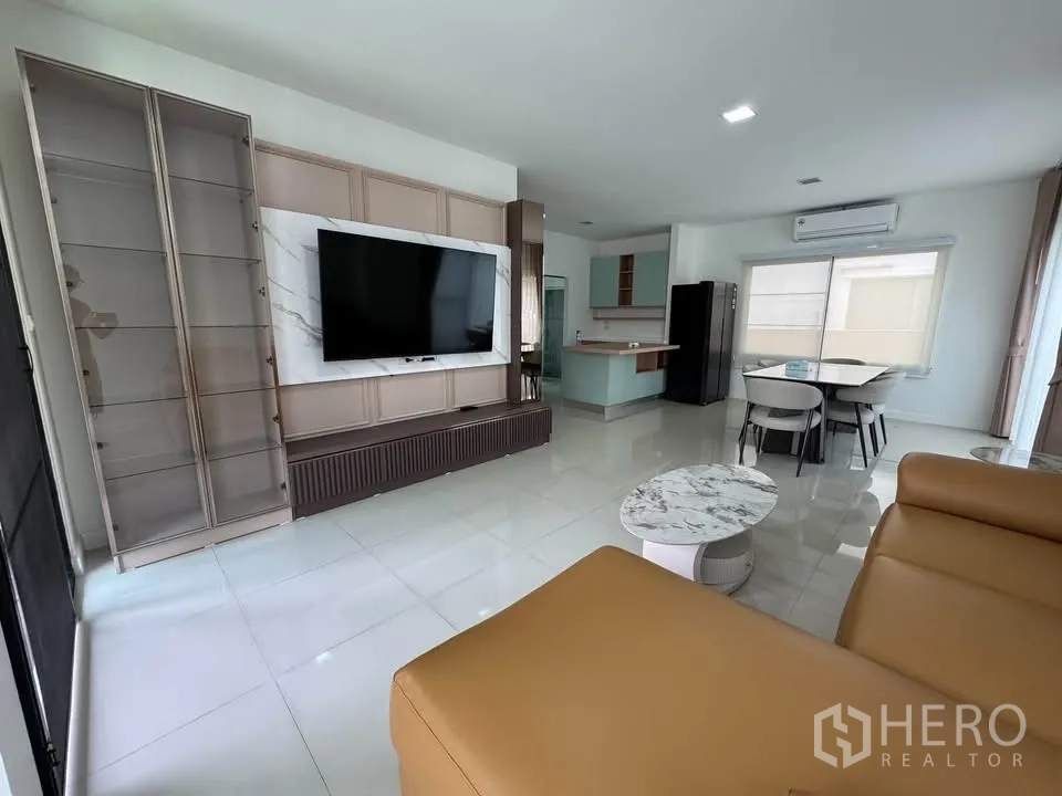 Detached House for rent in Prawet, Bangkok - Bright living room with wall-mounted TV, display cabinets, leather sofa, and marble coffee table.