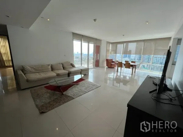 Condominium for rent in Watthana, Bangkok - Expansive open‑plan living area with L‑shaped sofa, glossy tiles and floor‑to‑ceiling windows facing the Bangkok skyline.