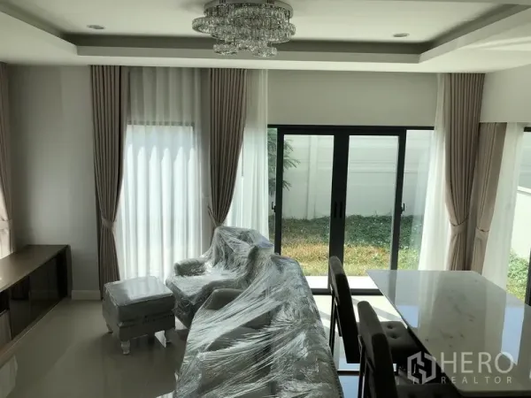 Detached House for rent in Prawet, Bangkok - Bright living room with floor-to-ceiling curtains, chandelier and sliding glass doors to the lawn.