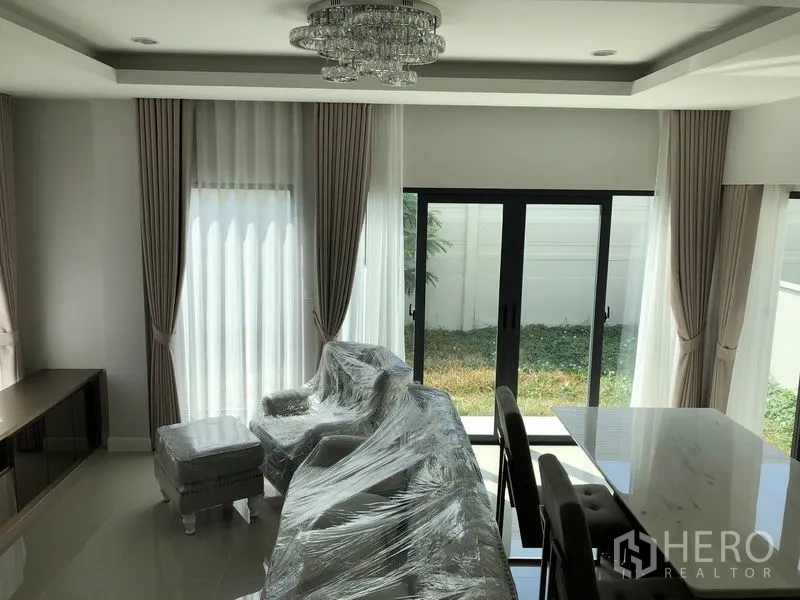 Detached House for rent in Prawet, Bangkok - Bright living room with floor-to-ceiling curtains, chandelier and sliding glass doors to the lawn.