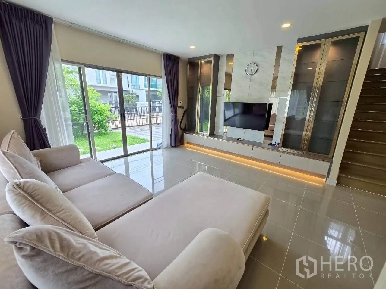 独栋房屋 for rent or sale in Lat Krabang, Bangkok - 客厅设转角沙发、内置电视墙与通向花园的推拉门。
