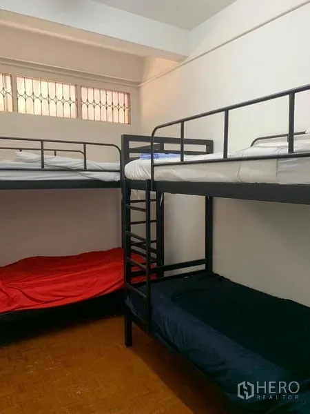 Shophouse for rent in Khlong Toei, Bangkok - Dorm-style bedroom with black metal bunk beds and a high window with security grilles.