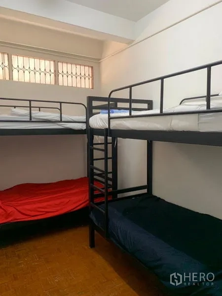 Shophouse for rent in Khlong Toei, Bangkok - Dorm-style bedroom with black metal bunk beds and a high window with security grilles.