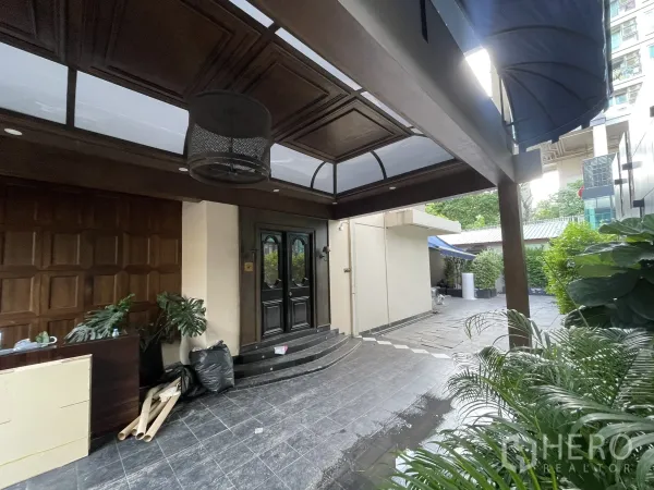 บ้าน ให้เช่า - เฉลียงหน้าบ้านมีหลังคาคลุม เพดานไม้มืดและประตูบานคู่ พร้อมต้นไม้กระถาง