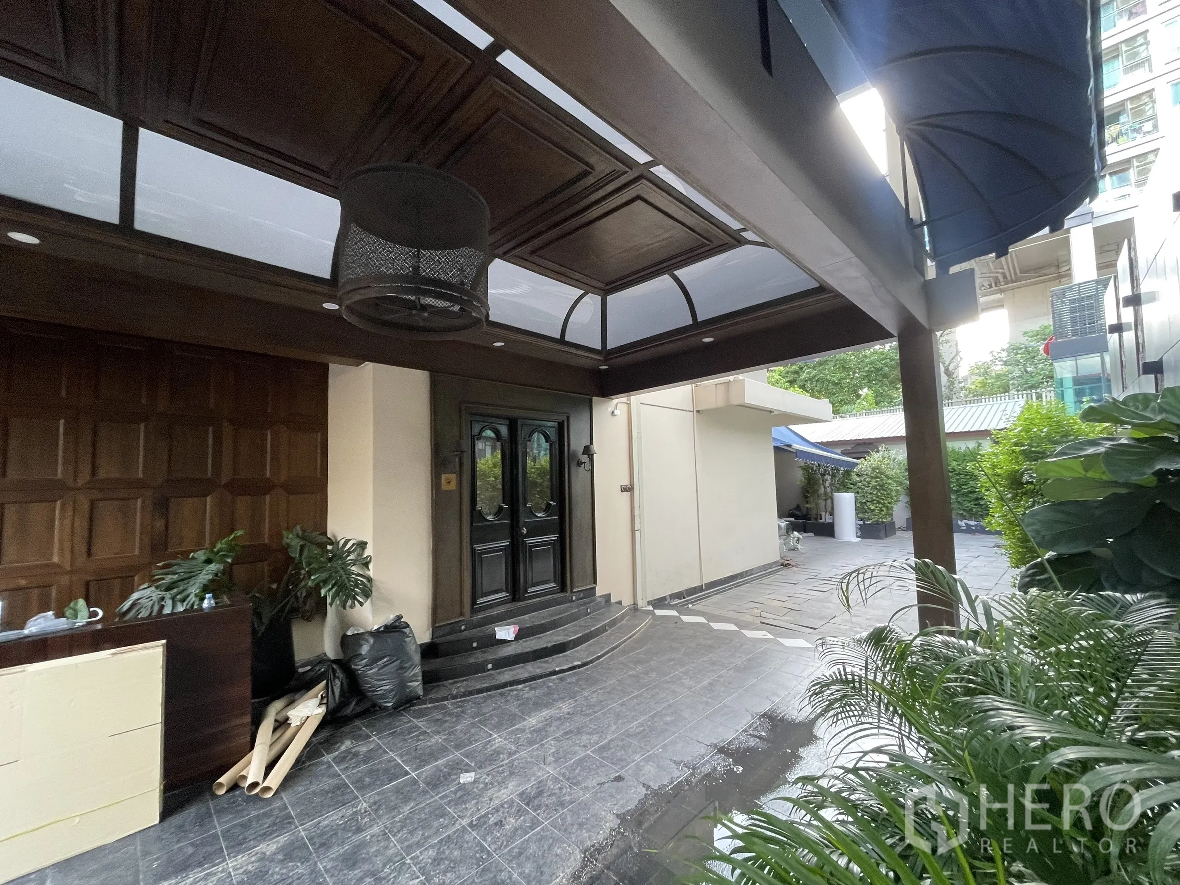 บ้าน ให้เช่า - เฉลียงหน้าบ้านมีหลังคาคลุม เพดานไม้มืดและประตูบานคู่ พร้อมต้นไม้กระถาง