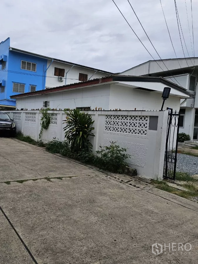 Detached House for rent or sale in Lat Phrao, Bangkok - Street-side view of the white perimeter wall and metal gate to the property.
