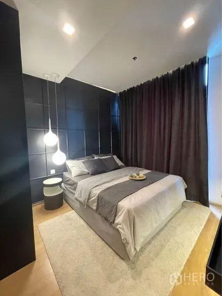 公寓 出租在Watthana, Bangkok - 温馨卧室，深色方格软包背景墙，吊灯与灰色床品，配遮光窗帘。