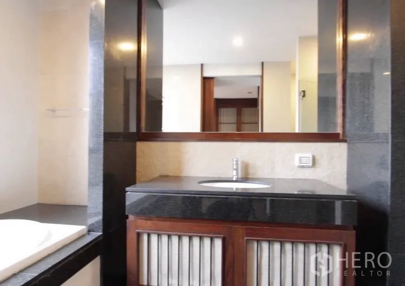 Detached House for rent in Khlong Toei, Bangkok - Contemporary bathroom with a wide mirror, dark stone countertop and wooden vanity cabinetry.