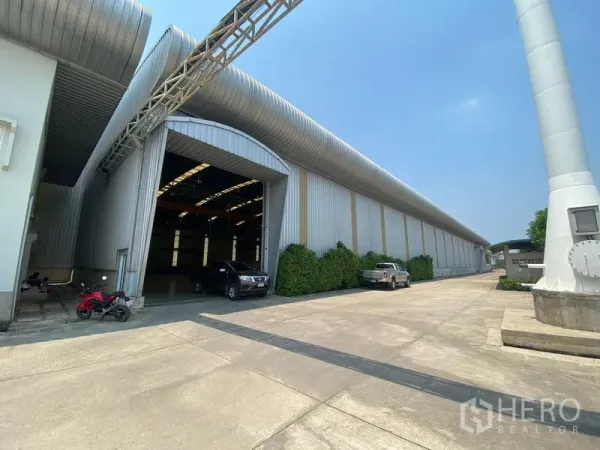 โรงงาน ให้เช่าหรือขายในSamut Sakhon - ภายนอกโรงงานที่บ้านแพ้ว สมุทรสาคร พร้อมลานคอนกรีตกว้าง ทางเข้าโหลดสินค้า และท่อระบายอากาศโลหะ.