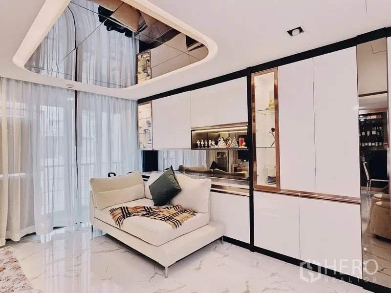 Condominium for sale in Bang Rak, Bangkok - Bright Silom condo living room with mirrored ceiling, white built-ins, sheer curtains and marble floor.