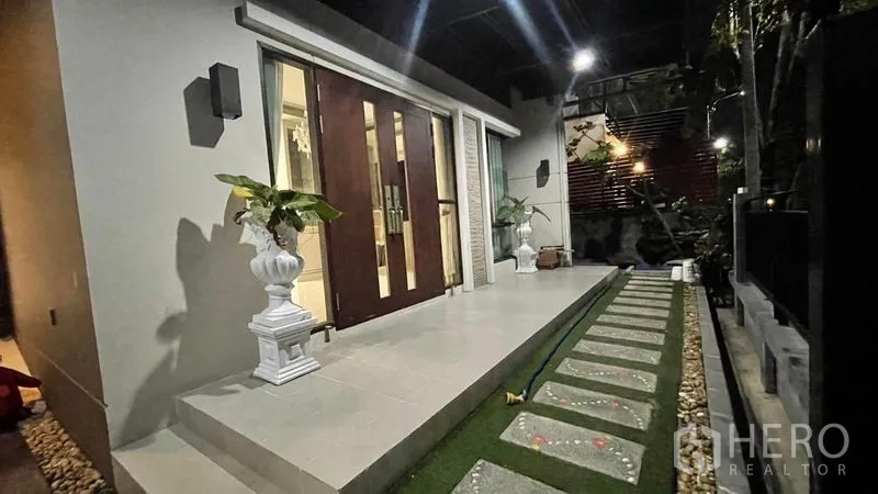 บ้าน ให้เช่าหรือขายในPrawet, Bangkok - มุมมองตอนกลางคืนของระเบียงหน้าบ้าน ประตูไม้คู่ ทางขึ้นกระเบื้อง ทางเดินแผ่นทาง และกระถางต้นไม้