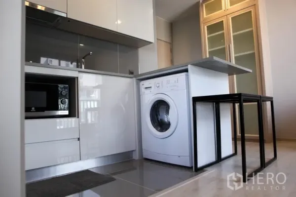 Condominium for rent in Watthana, Bangkok - Compact condo kitchen with built-in microwave and front-loading washer under the countertop.