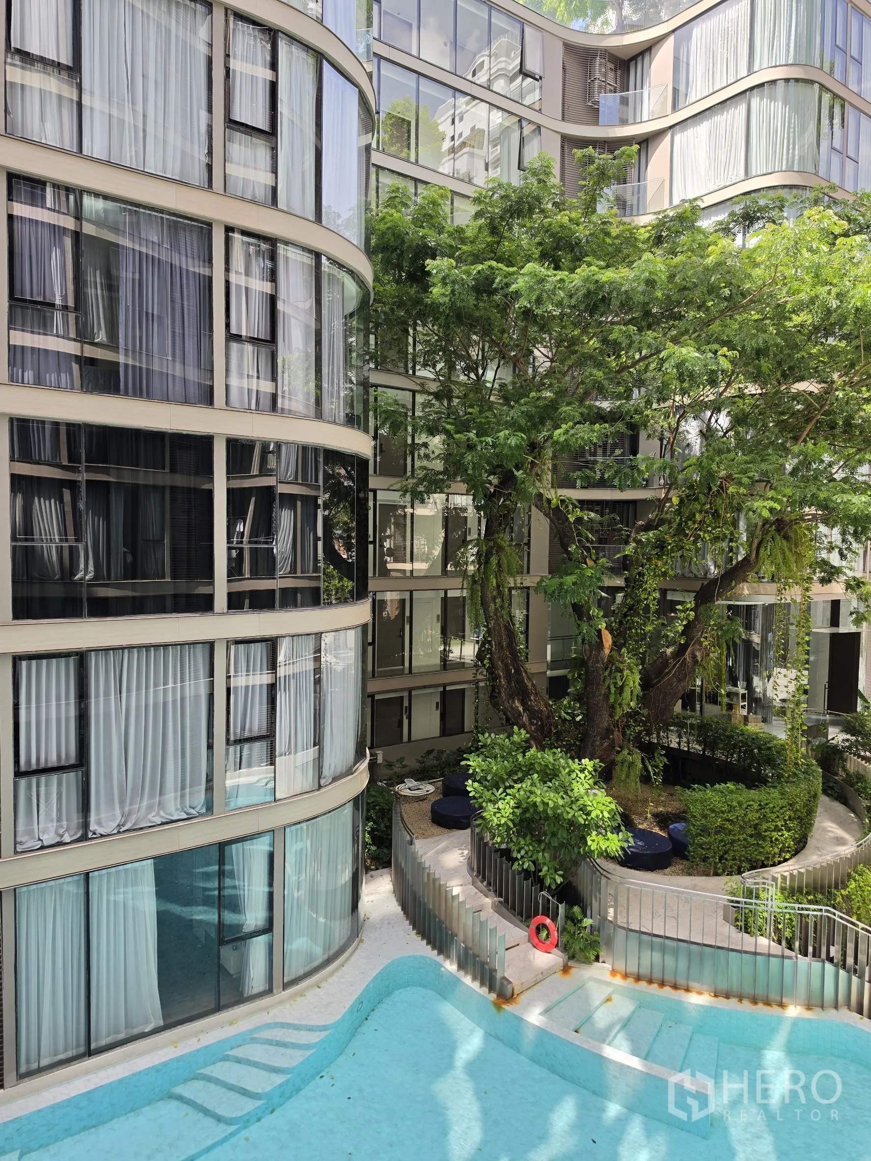 Condominium for rent in Khlong Toei, Bangkok - Courtyard swimming pool surrounded by trees and curved glass buildings.