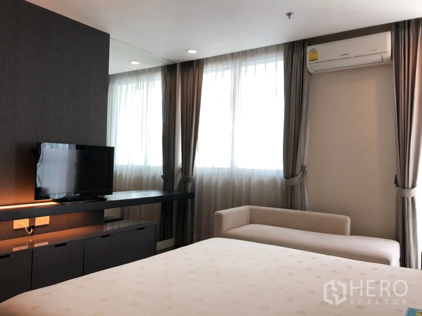 公寓 出租在Pathum Wan, Bangkok - 主卧影音墙，电视柜、长置物台、沙发长凳与带窗帘的窗户。