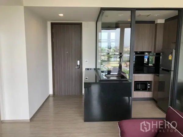 Condominium for rent in Watthana, Bangkok - Entry hall facing a glass‑enclosed kitchen with black stone countertop, wood cabinetry, and appliances.