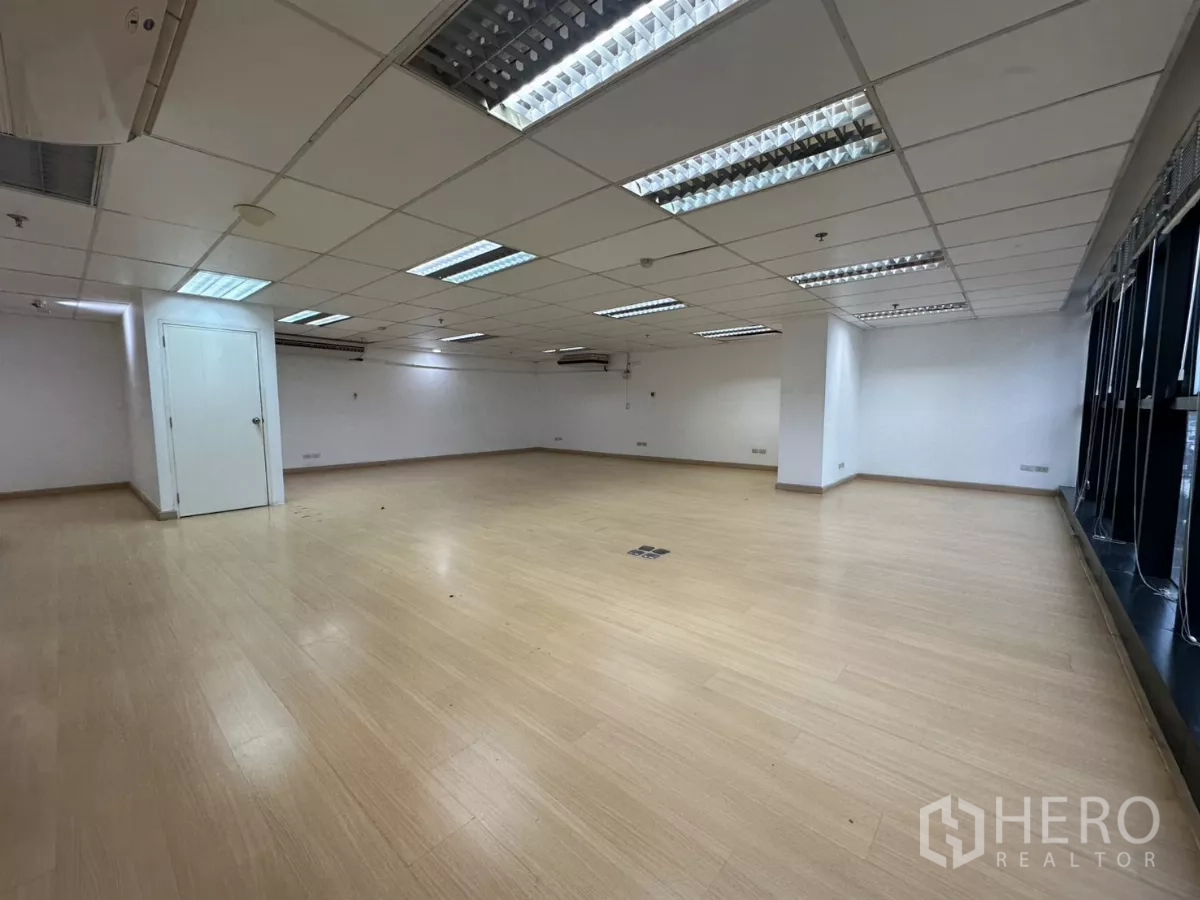 Office Space for rent in Watthana, Bangkok - Bright open workspace with fluorescent lighting, wood floors and a side storage door.