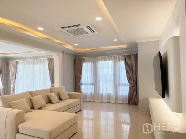 Detached House for rent or sale in Bang Phli, Samut Prakan - Bright living room with L-shaped beige sofa, recessed lighting and sheer curtains.