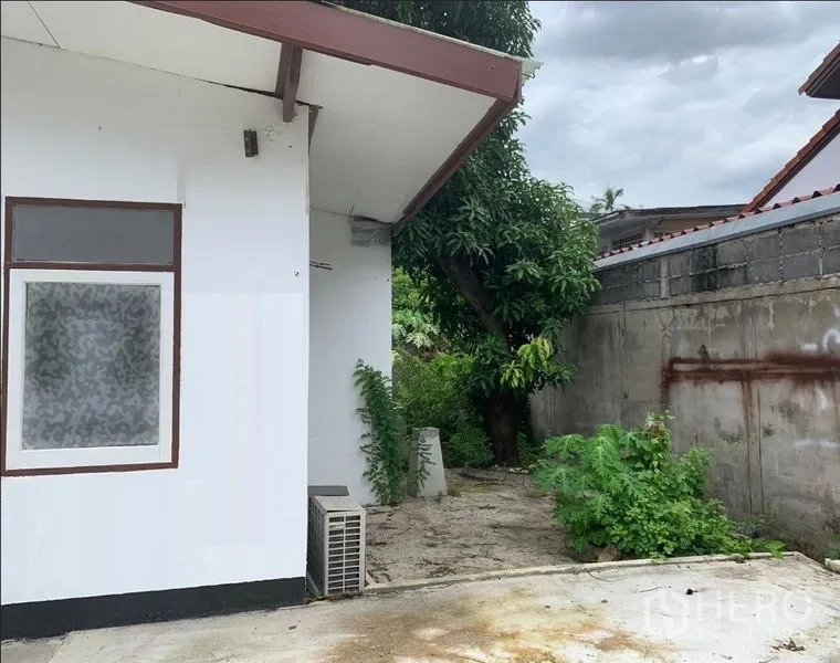 Detached House for rent in Phra Khanong, Bangkok - Side of the house with window, outdoor AC unit, tree and boundary wall.