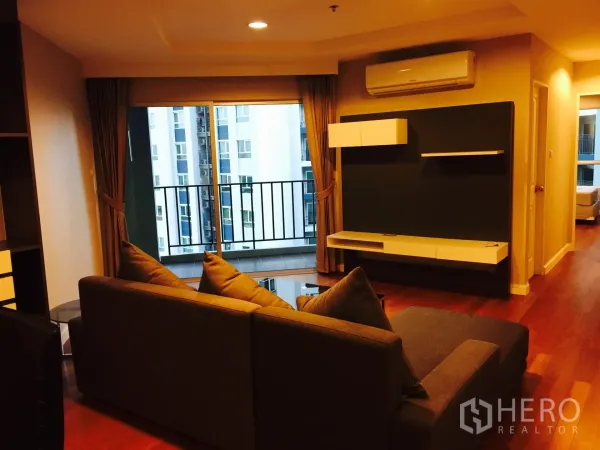 คอนโด ให้เช่าในHuai Khwang, Bangkok - ห้องนั่งเล่นอบอุ่น โซฟาตัวแอล พื้นไม้ และระเบียงมองเห็นอาคารเมือง