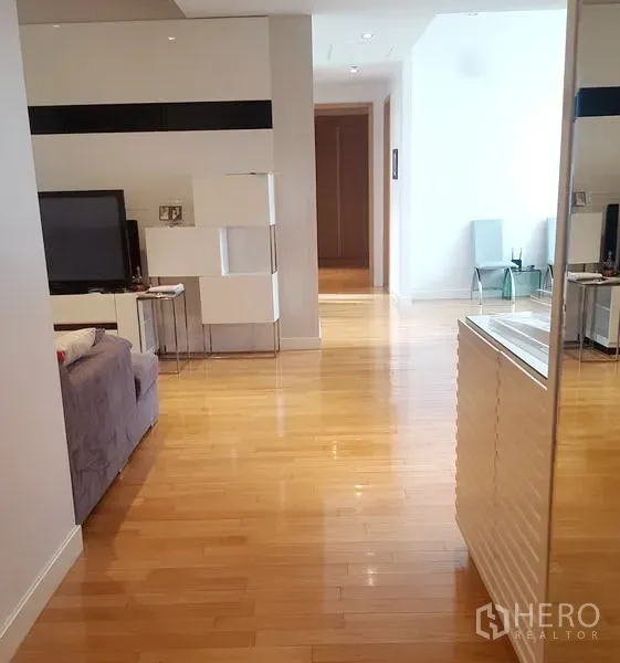 Condominium for rent in Khlong Toei, Bangkok - Bright open-plan living area with light wood flooring, TV console and hallway view.