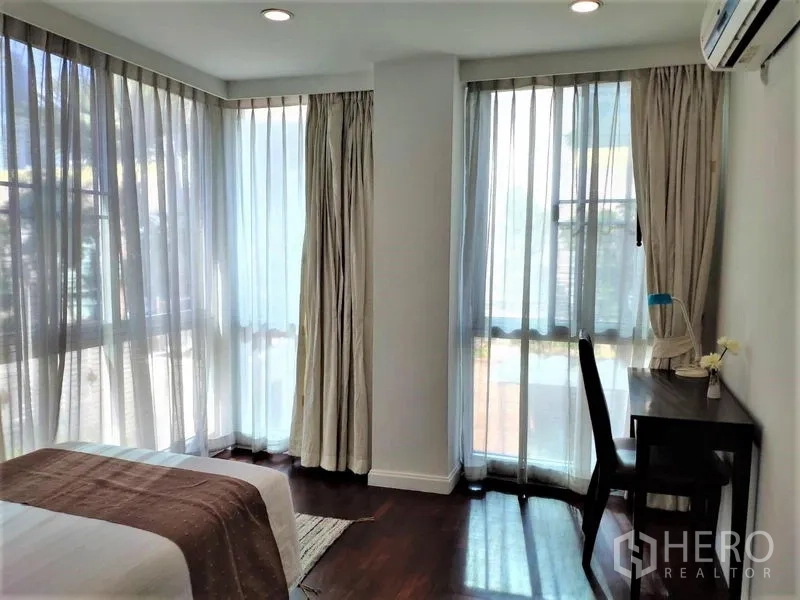 Condominium for rent in Bang Rak, Bangkok - Bright corner bedroom with a desk and wraparound windows.