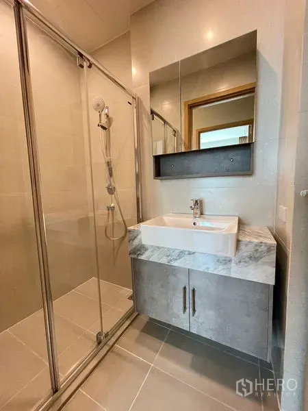 Condominium for rent in Watthana, Bangkok - Modern bathroom with glass-enclosed shower and square basin on a marble counter.