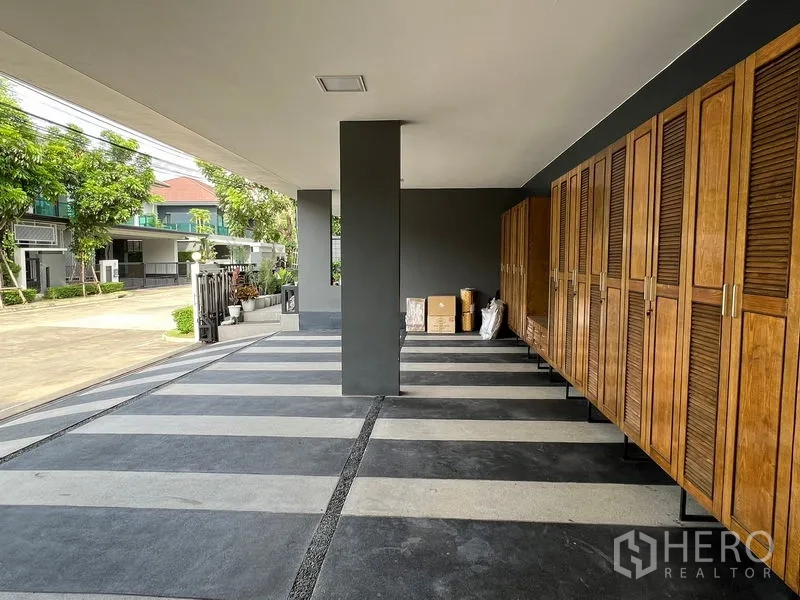Detached House for sale in Bang Kapi, Bangkok - Covered carport with striped concrete floor and a long row of wooden storage cabinets.