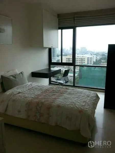 Condominium for rent in Phaya Thai, Bangkok - Cozy bedroom with bed, built‑in desk and floor‑to‑ceiling window showing Bangkok city view.