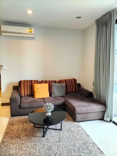 Condominium for rent in Watthana, Bangkok - Living room with sectional sofa, round coffee table and textured rug.