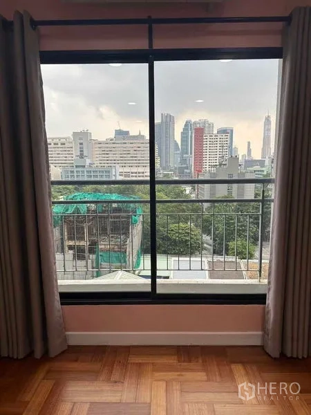 Condominium for sale in Bangkok - City skyline and greenery seen through a sliding window with curtains.
