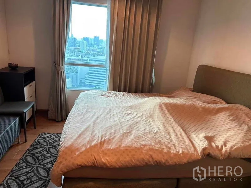 คอนโด ขายในHuai Khwang, Bangkok - ห้องนอนเตียงขนาดใหญ่ ผ้าม่านสูงเต็มบาน พร้อมหน้าต่างเห็นวิวเมืองกรุงเทพฯ