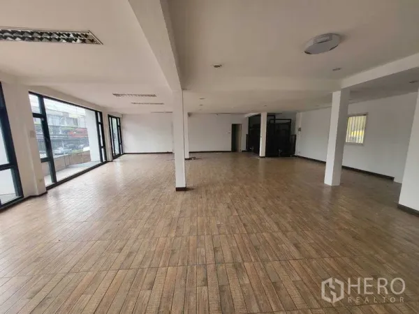 Shophouse for rent in Khlong Toei, Bangkok - Spacious upper floor with wood-look flooring and large corner windows overlooking the street.