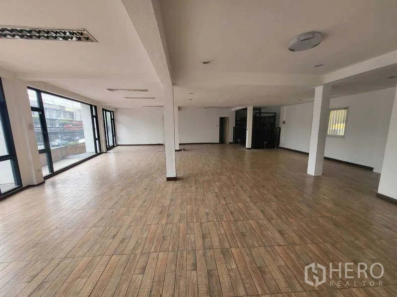 Shophouse for rent in Khlong Toei, Bangkok - Spacious upper floor with wood-look flooring and large corner windows overlooking the street.