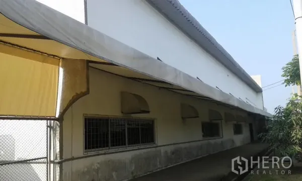 Factory for rent in Uthai, Phra Nakhon Si Ayutthaya - Side walkway of the factory showing long awnings, barred windows and a chain‑link gate.