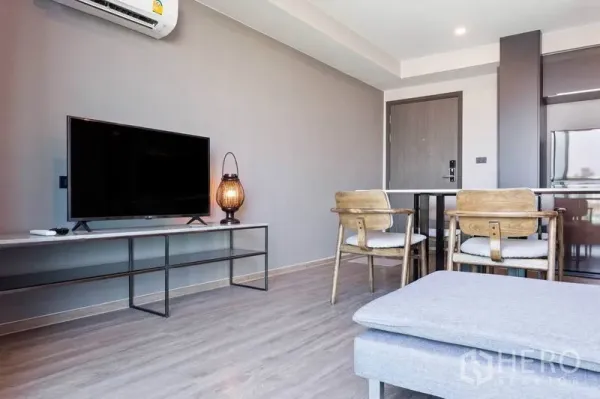 Condominium for rent or sale in Watthana, Bangkok - Open-plan living area with TV console, dining set and wood floors beside the kitchenette.