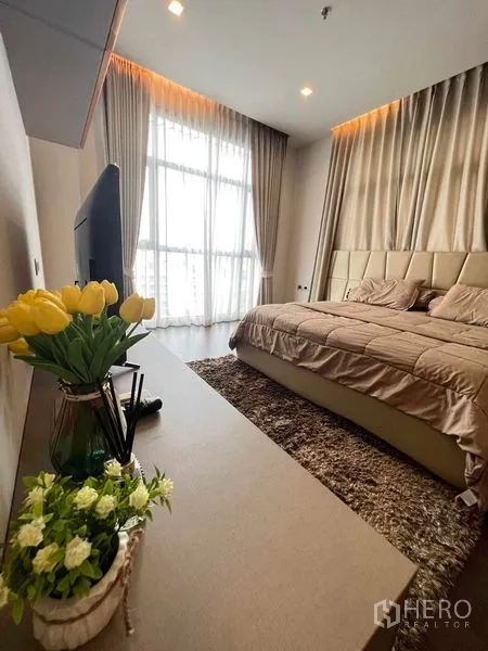 Condominium for rent or sale in Watthana, Bangkok - Master bedroom with warm lighting, large window, beige bedding and plush area rug.