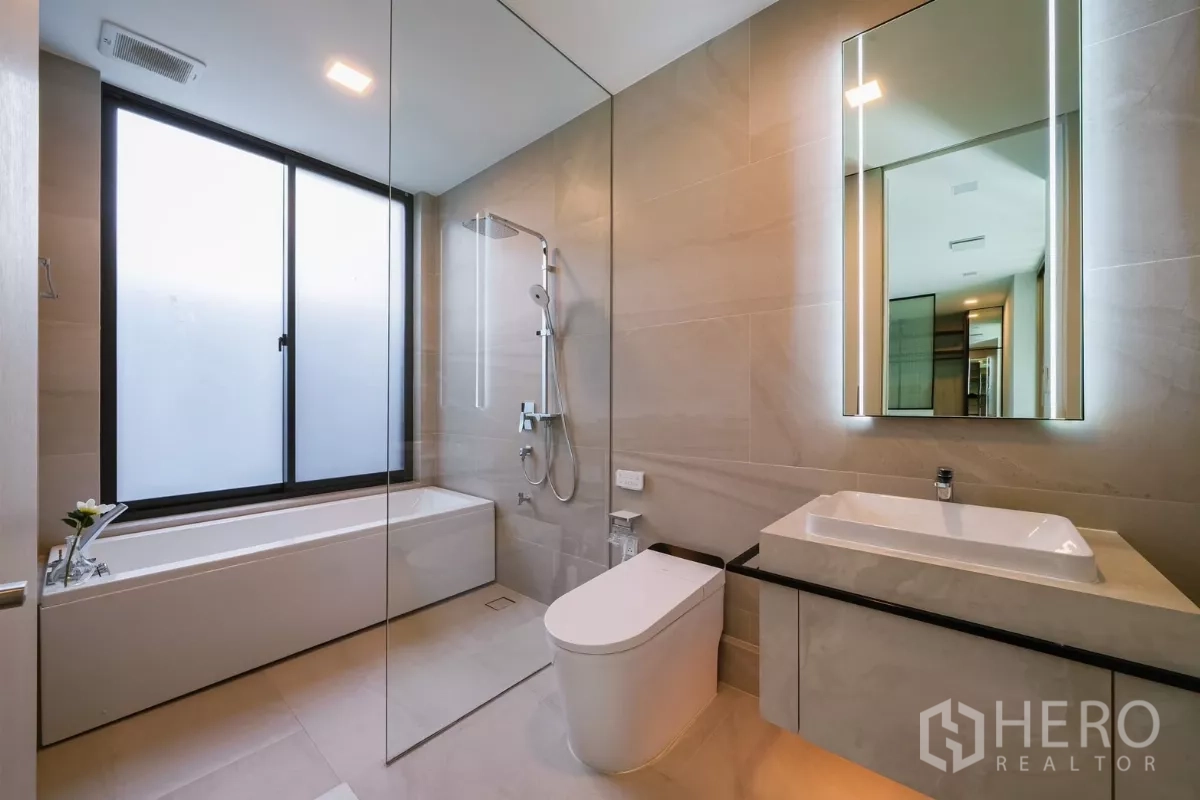 Detached House for rent or sale in Saphan Sung, Bangkok - Bright bathroom with bathtub, glass shower enclosure and backlit mirror.