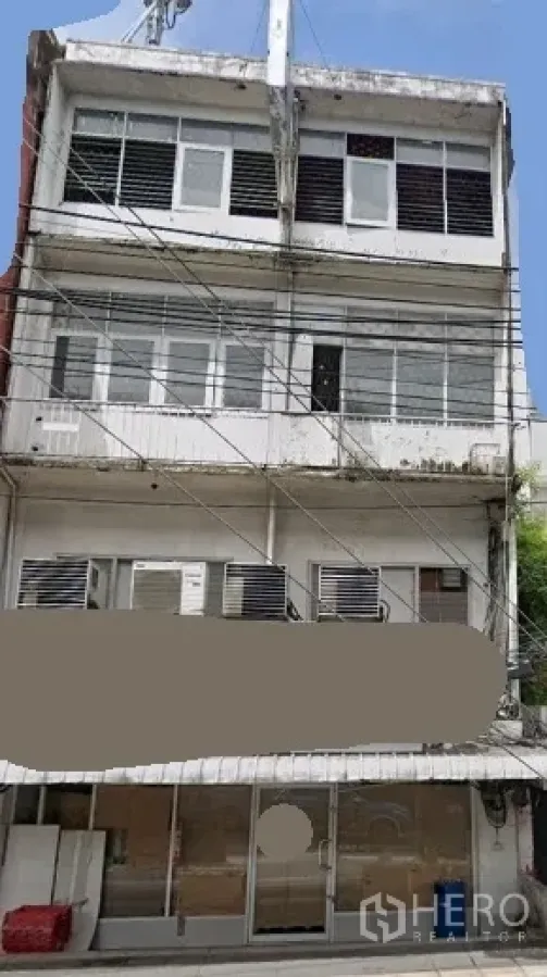 Shophouse for rent in Khlong Toei, Bangkok - Four-storey shophouse exterior with wide glass storefront, upper-floor windows, balconies, multiple AC units and overhead utility lines in Khlong Toei near BTS Phra Khanong.