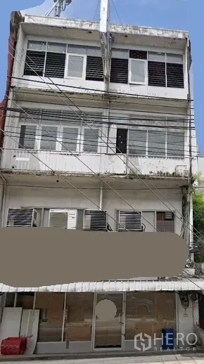 Shophouse for rent in Khlong Toei, Bangkok - Four-storey shophouse exterior with wide glass storefront, upper-floor windows, balconies, multiple AC units and overhead utility lines in Khlong Toei near BTS Phra Khanong.