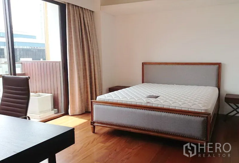 Condominium for sale in Pathum Wan, Bangkok - Sunny master bedroom with upholstered bedframe, wood floors and balcony access.