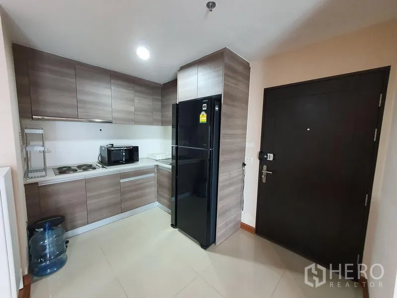คอนโด ให้เช่าในHuai Khwang, Bangkok - ครัวยูโรบิวท์อิน ตู้ลายไม้ เตาไฟฟ้า ไมโครเวฟ และตู้เย็นสีดำขนาดใหญ่ ใกล้ประตูทางเข้า