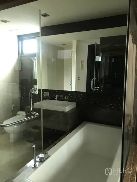 Condominium for rent in Watthana, Bangkok - Bathroom with soaking bathtub, glass partition, toilet and vanity in a modern Bangkok condominium.