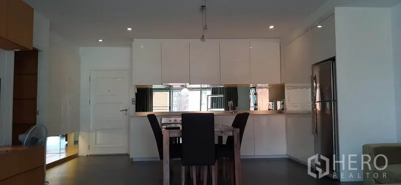 Condominium for rent in Phaya Thai, Bangkok - Dining area for four facing a minimalist white kitchen with tall refrigerator.