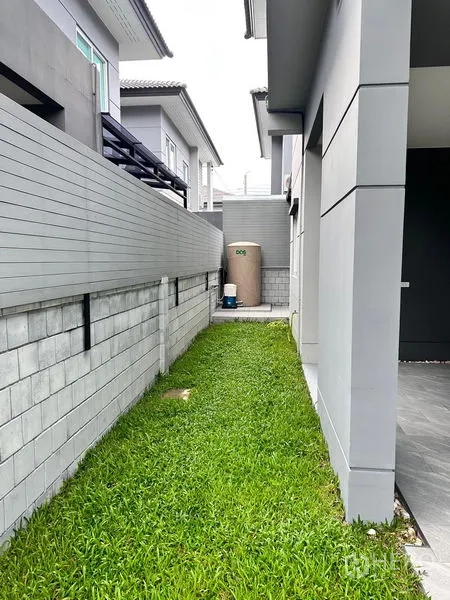独立式住宅 出售在Prawet, Bangkok - 房屋侧院狭长草坪，设水箱与铺装步道。