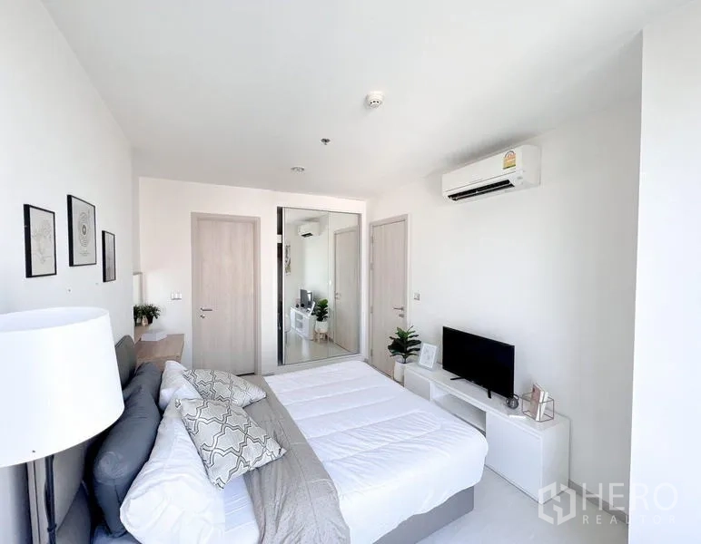 Condominium for rent or sale in Khlong Toei, Bangkok - Bedroom angle showing mirrored wardrobe, TV console and wall-mounted air conditioner.