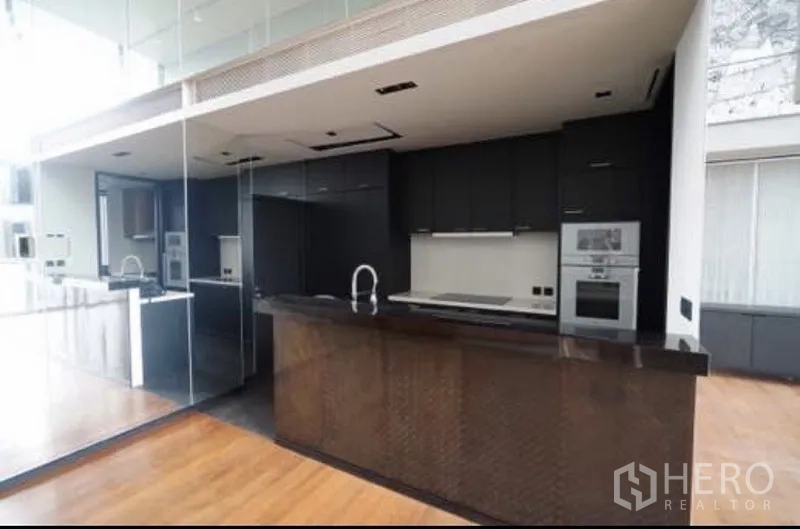 Condominium for rent in Sathon, Bangkok - Modern main kitchen with black cabinetry, white countertops, built-in oven and a sleek peninsula.